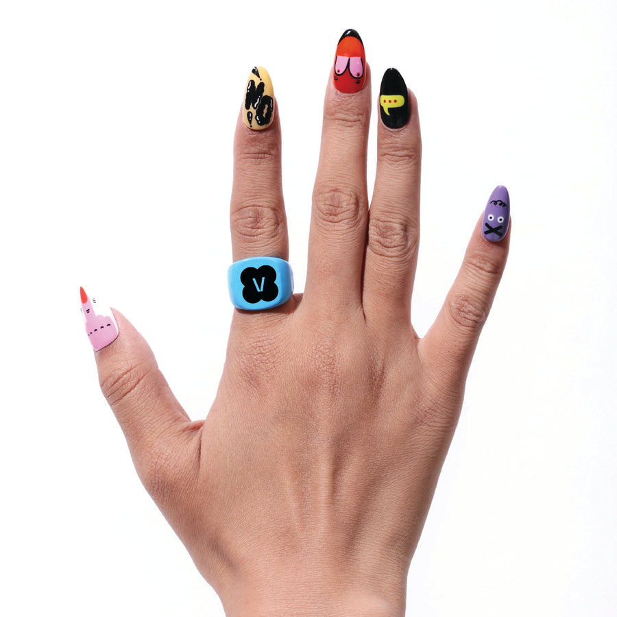 Hand with colorful, artist-designed press-on nails and a blue ring with a black 'V' symbol.